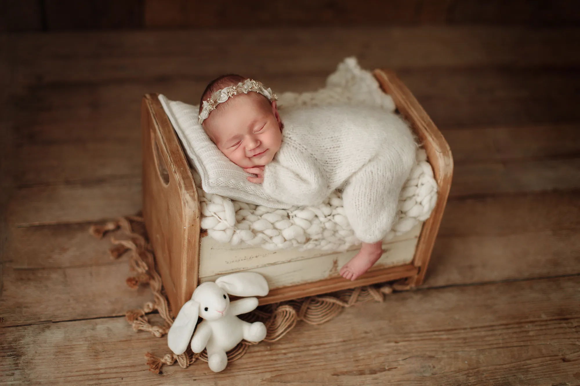 Newborn baby asleep in a small wooden bed with a toy bunny