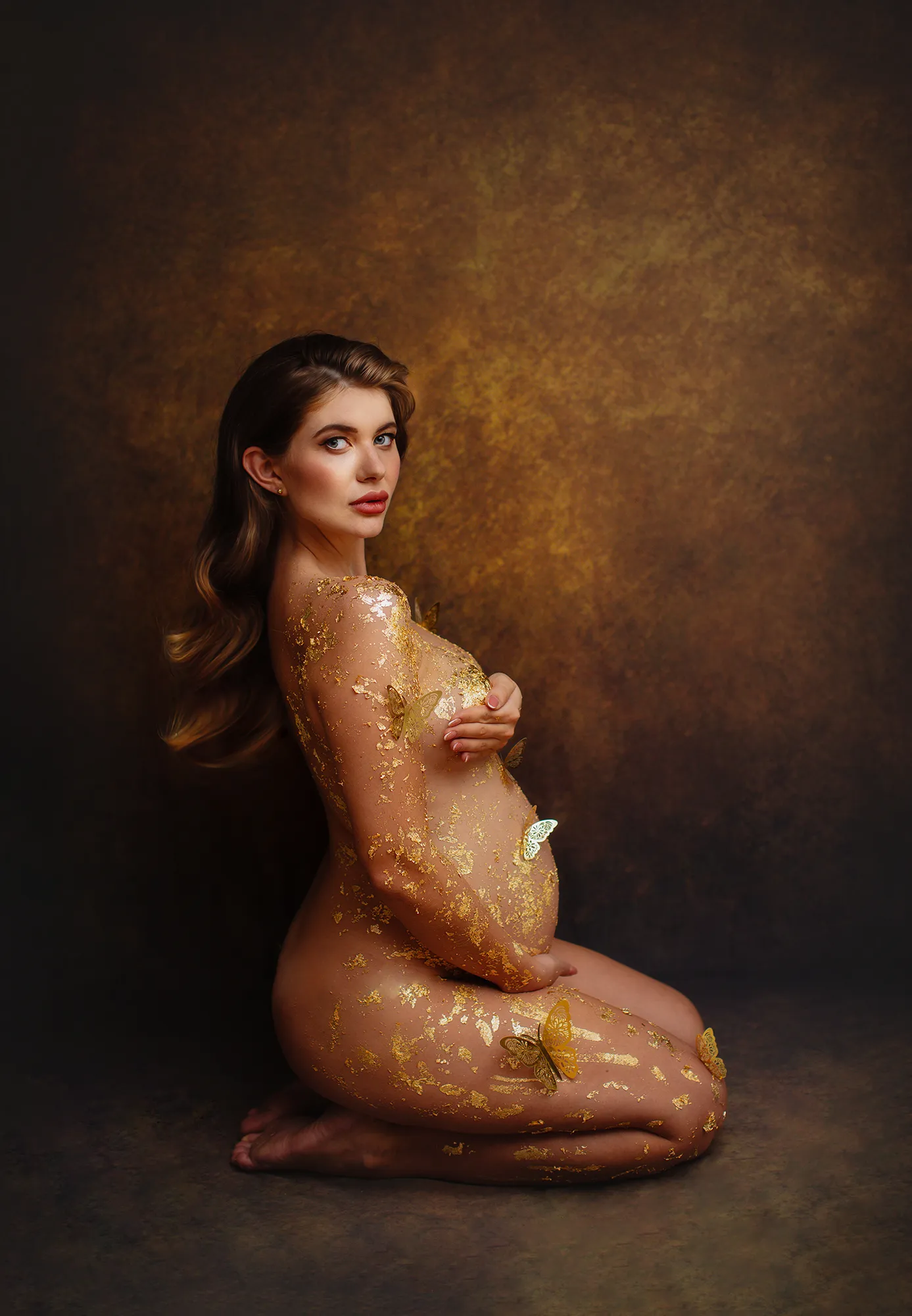 Pregnant woman kneeling with gold leaf on her bump, fine art maternity portrait