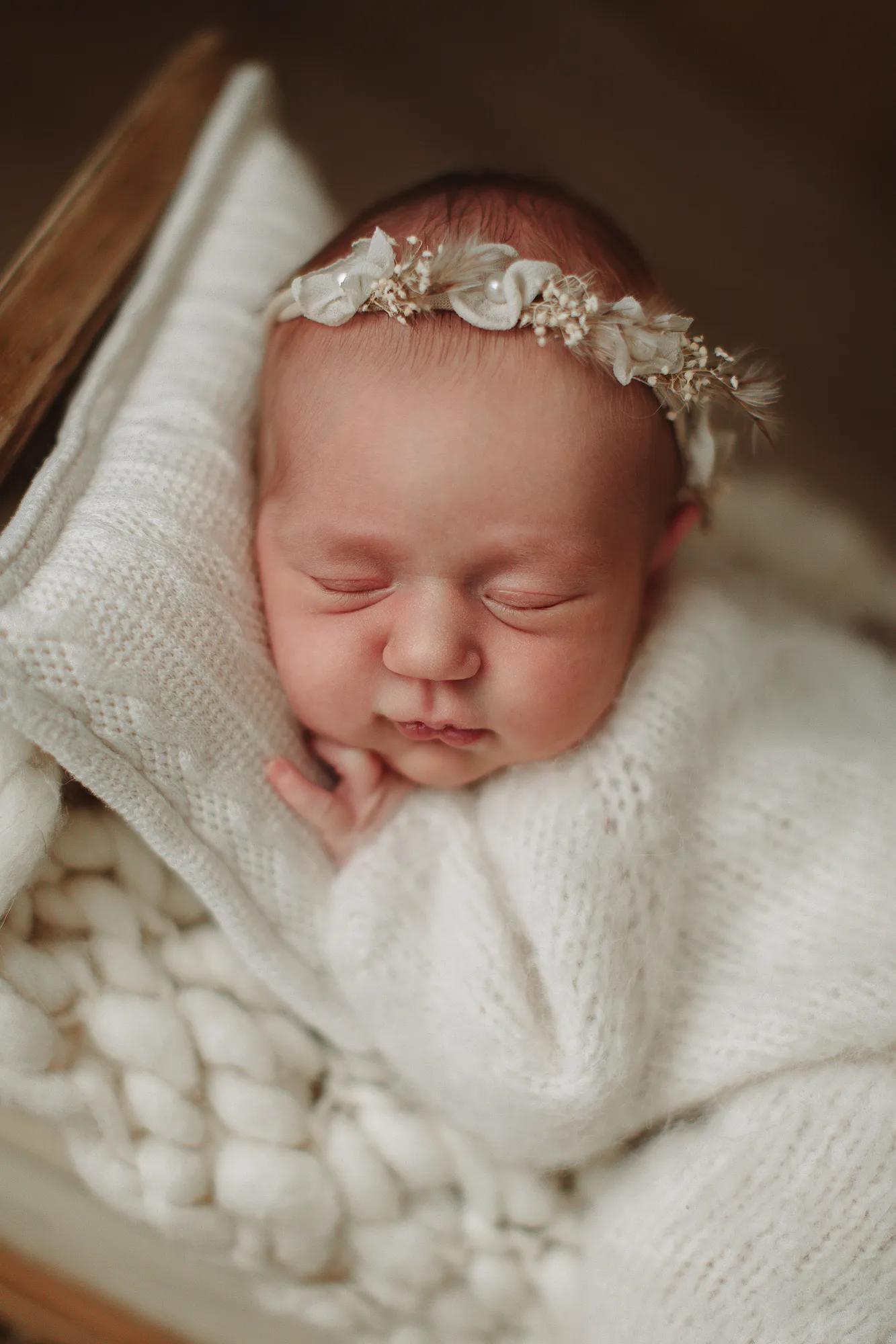Close-up of a newborn baby with a flower headband on a cream knit blanket