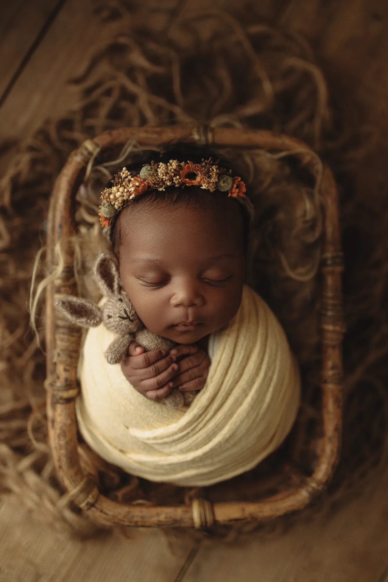 Newborn swaddled in pale yellow with a toy bunny in a woven basket