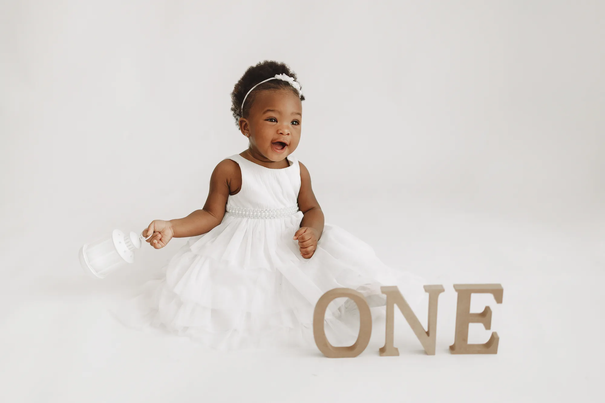 The birthday girl in a white tulle dress sitting beside wooden ONE letters