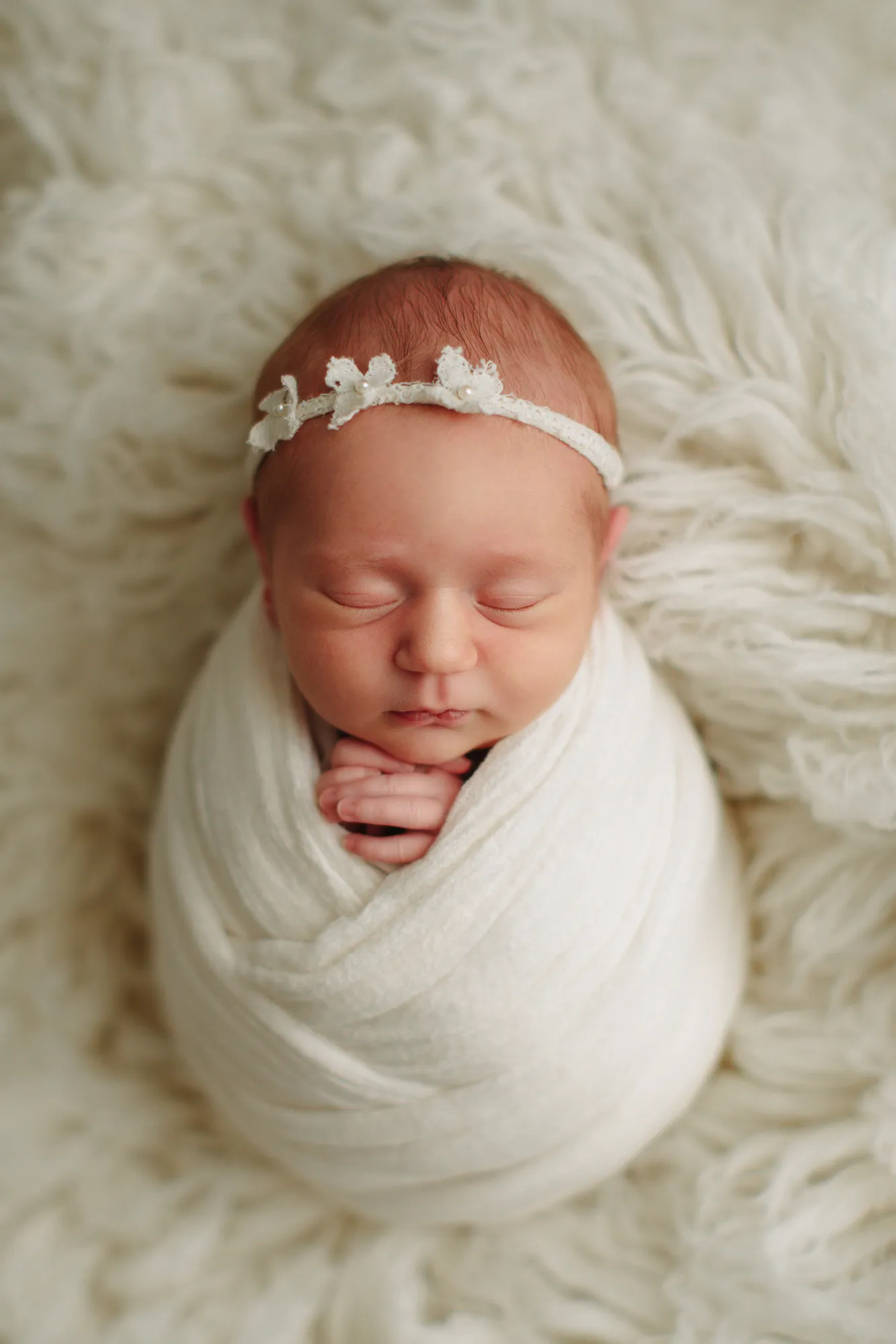 Newborn baby swaddled in cream with a floral headband on cream fur