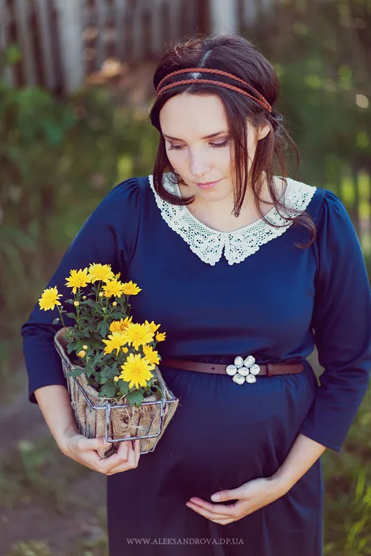 Pregnant woman in a navy dress holding yellow flowers outdoors