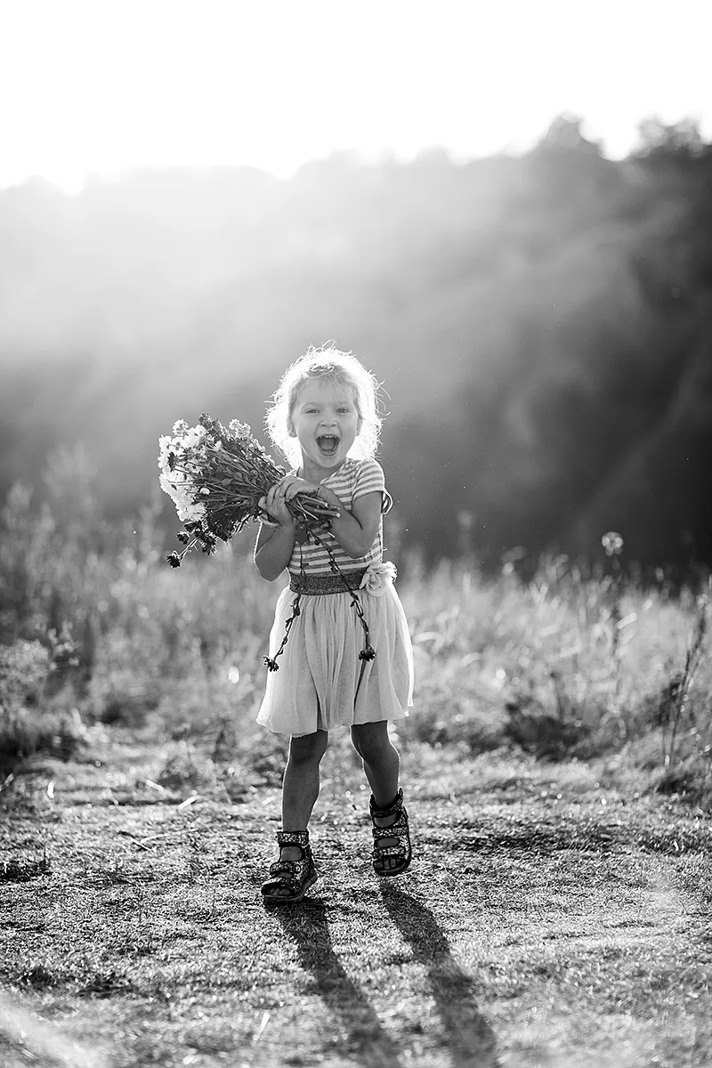 Black and white photo of a laughing girl holding wildflowers