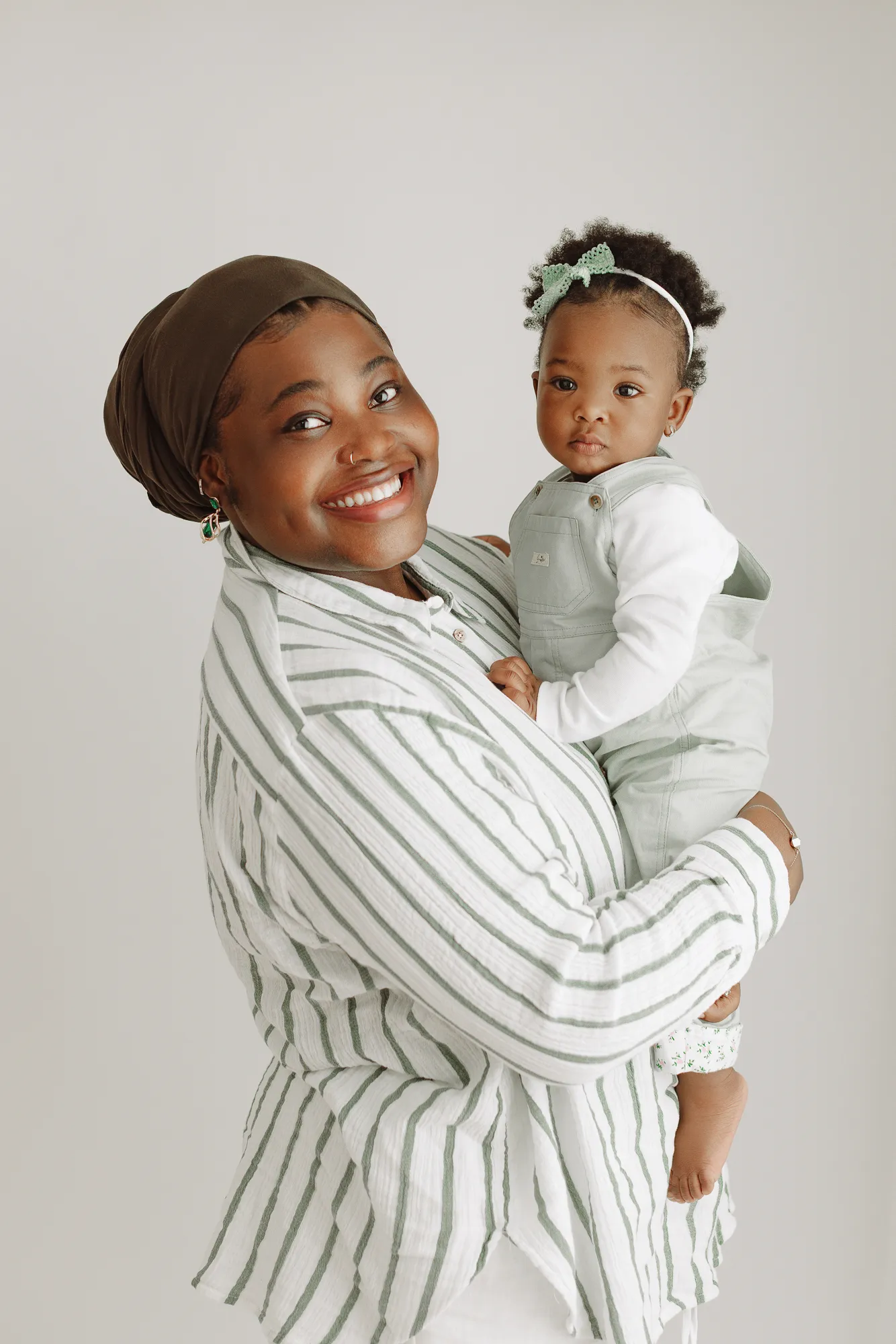 Mum smiling and holding her daughter in sage dungarees