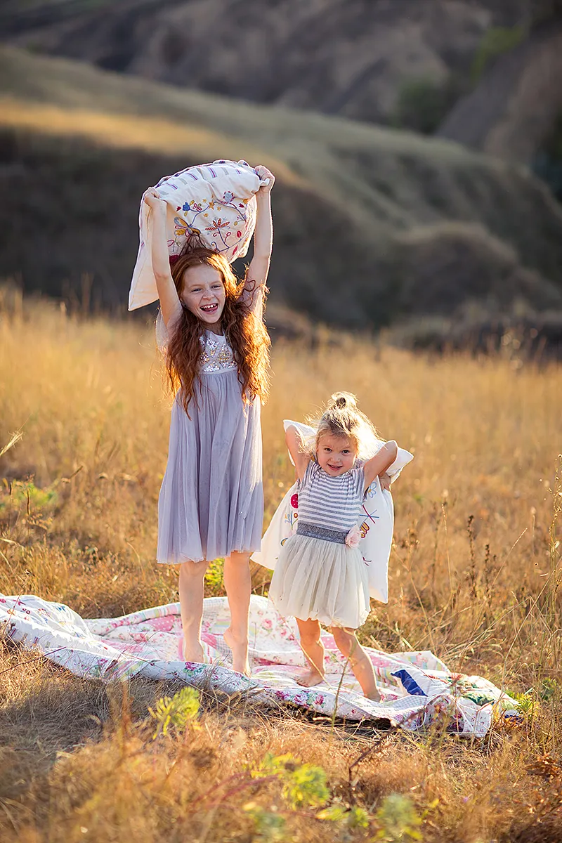 Two sisters playing with a blanket in a golden meadow