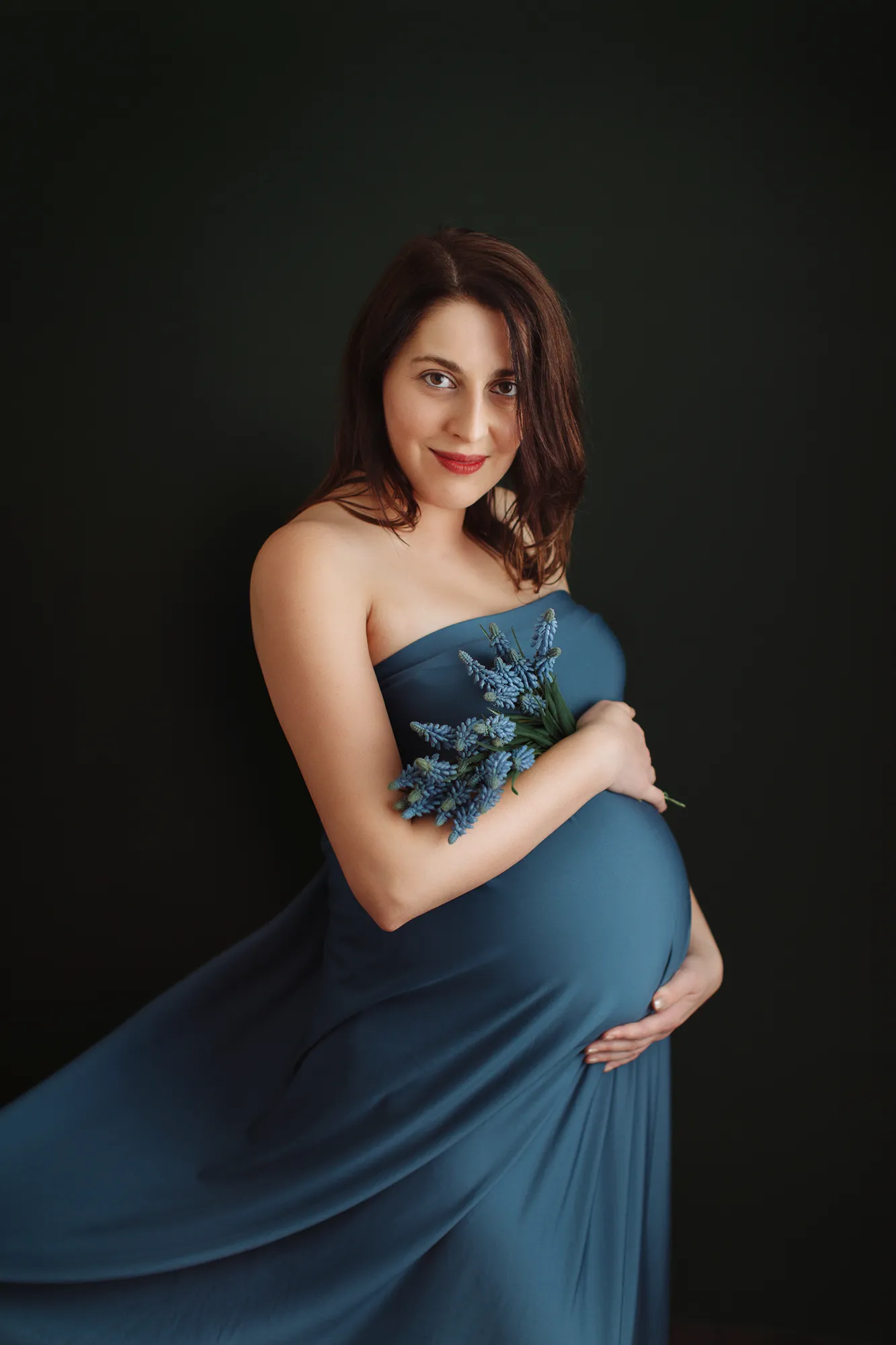 Pregnant woman in a teal off-shoulder dress holding a bouquet