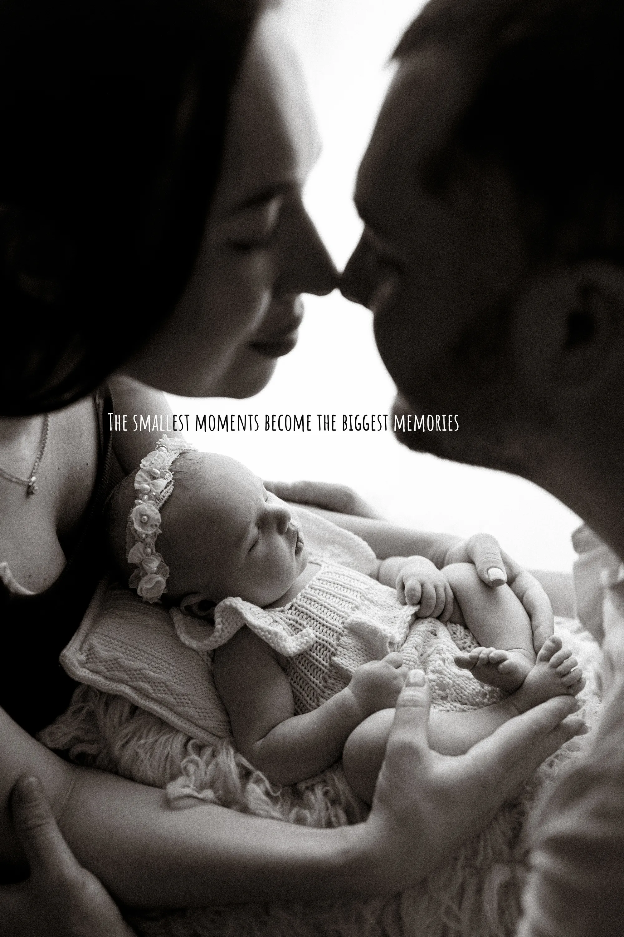 Black and white photo of parents about to kiss above their sleeping newborn