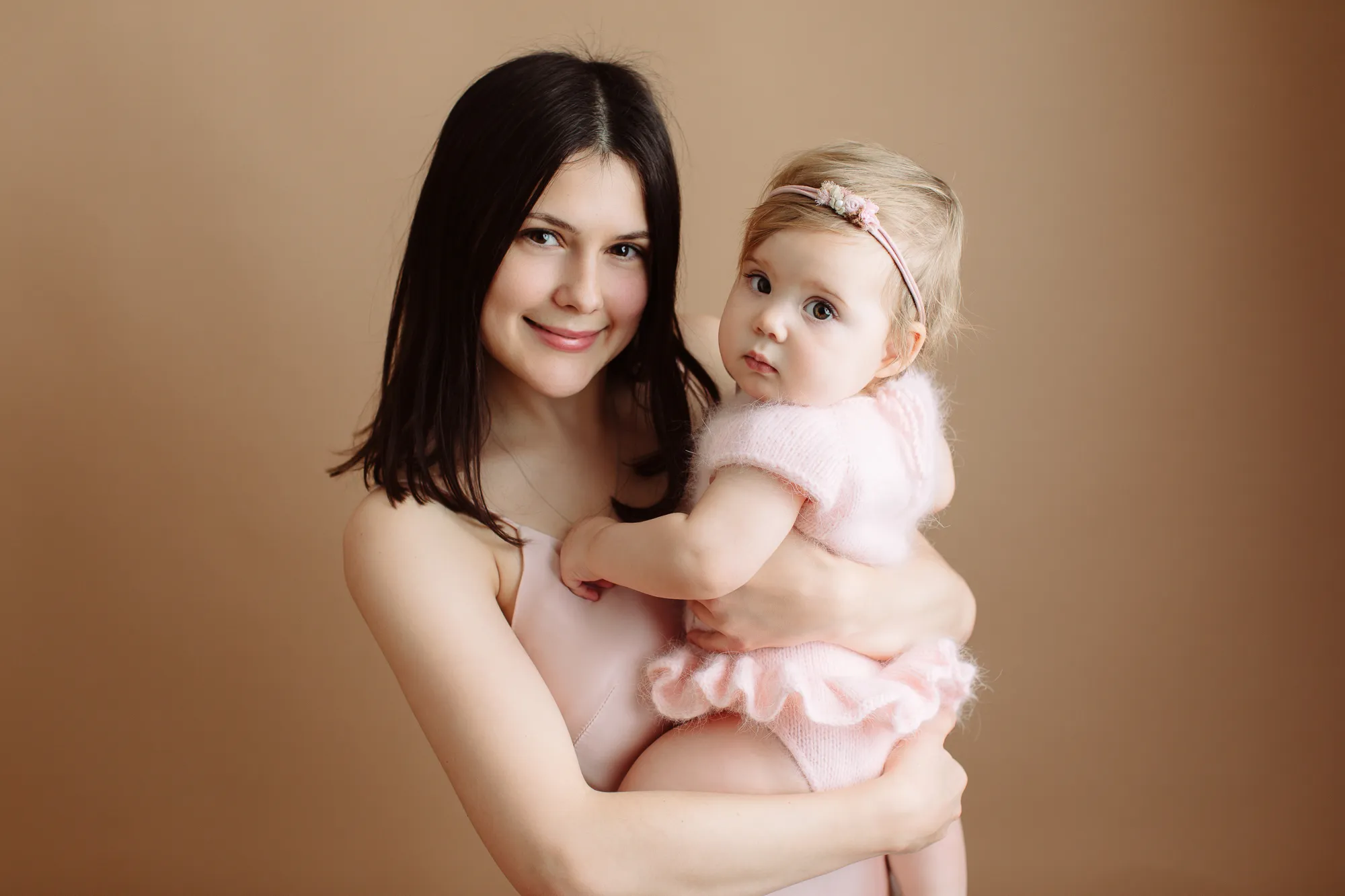 Smiling mother holding her baby daughter in a pink knit outfit