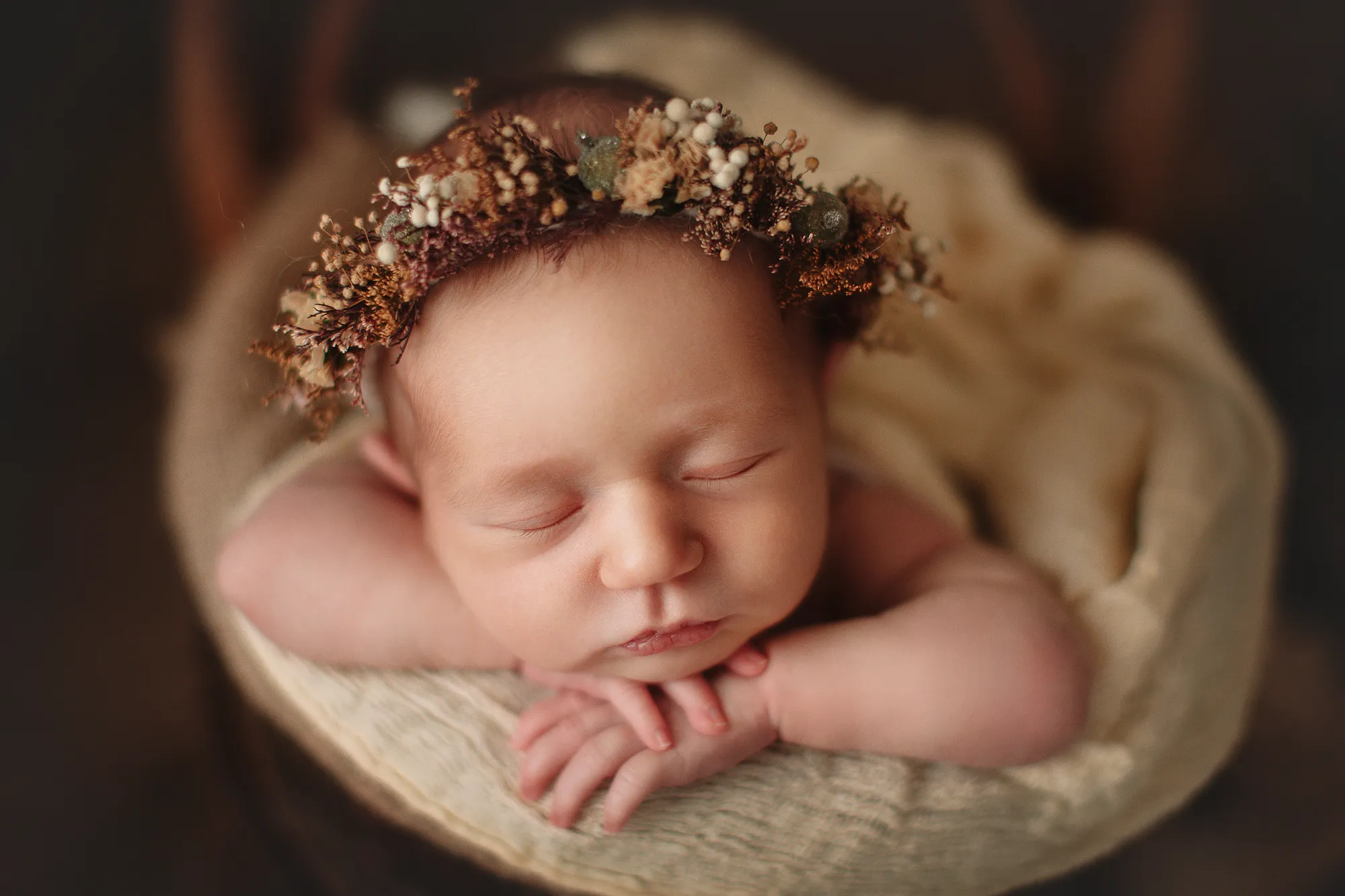 Close-up of a newborn with a dried-flower crown in a wooden bowl