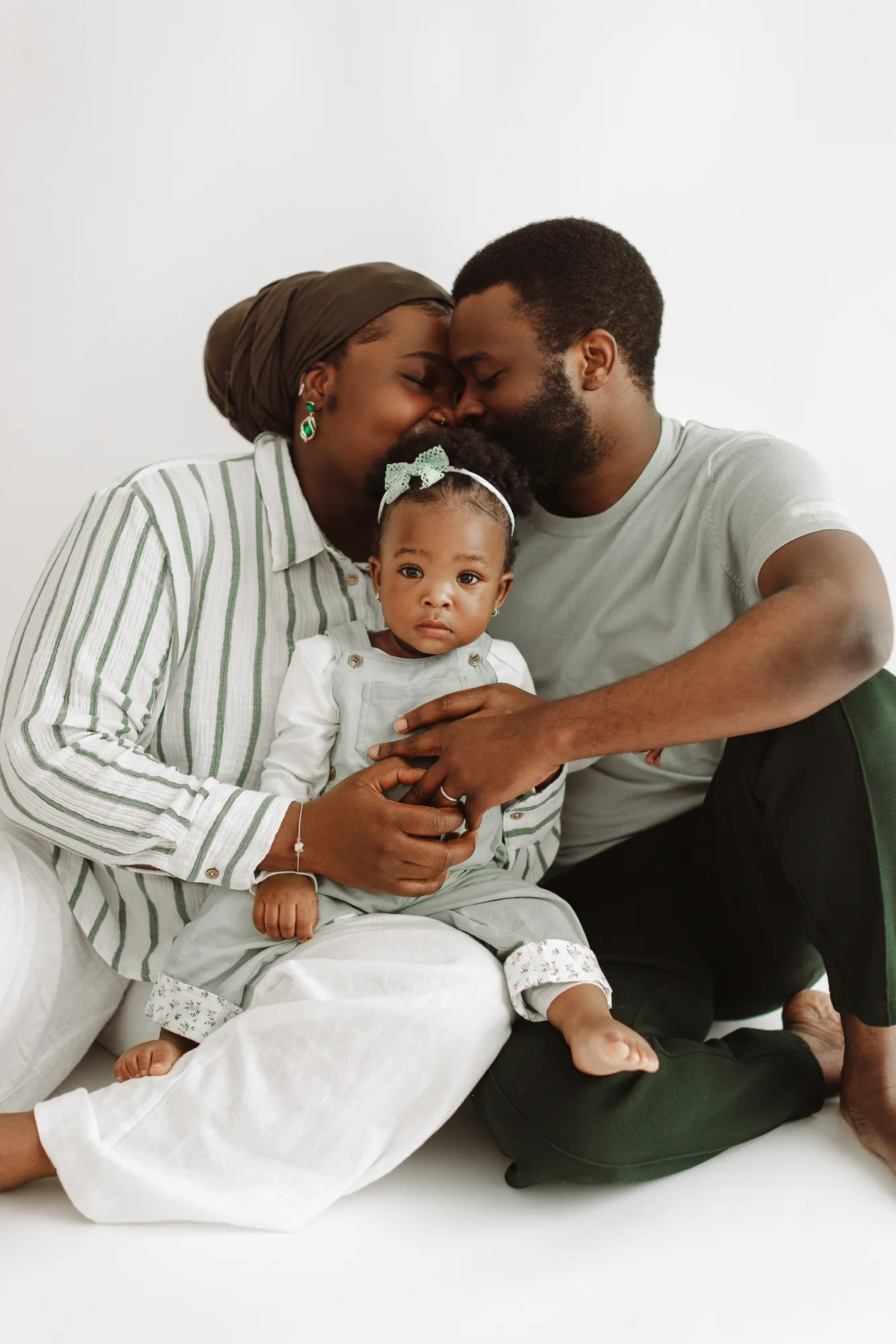 Parents kissing while cuddling their daughter on the studio floor