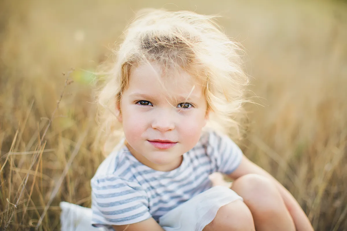 Close-up of a little girl with curly blonde hair in a sunny field