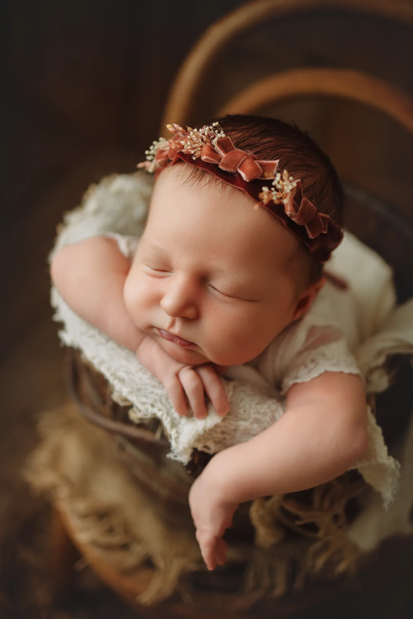 Sleeping newborn in a rustic bucket wearing a burgundy flower headband