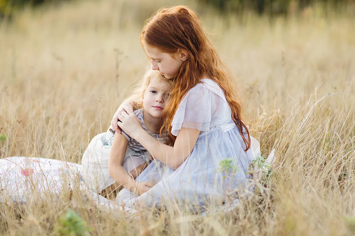 Big sister hugging her little sister in a golden meadow