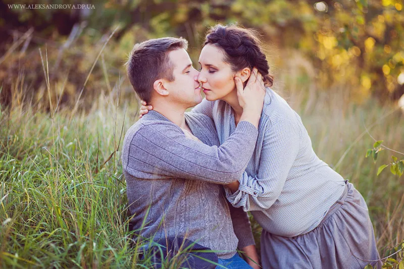 Expectant couple kissing in a grassy field