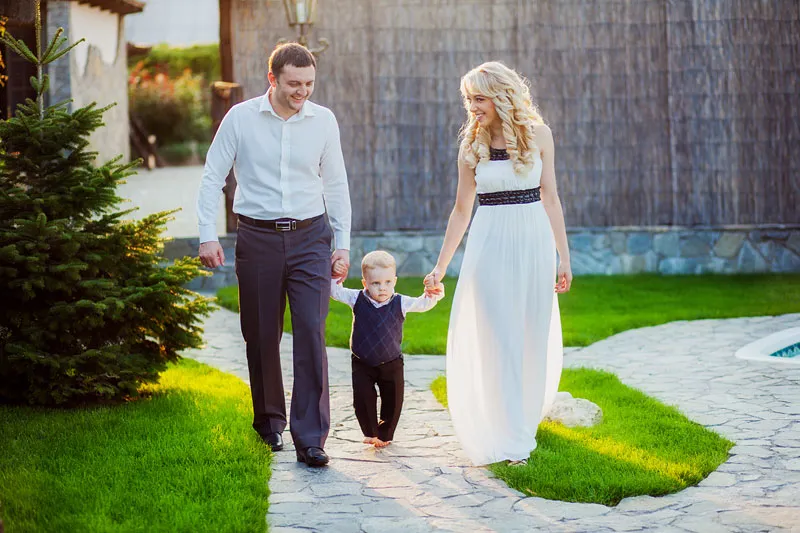 Parents walking hand in hand with their toddler son along a garden path