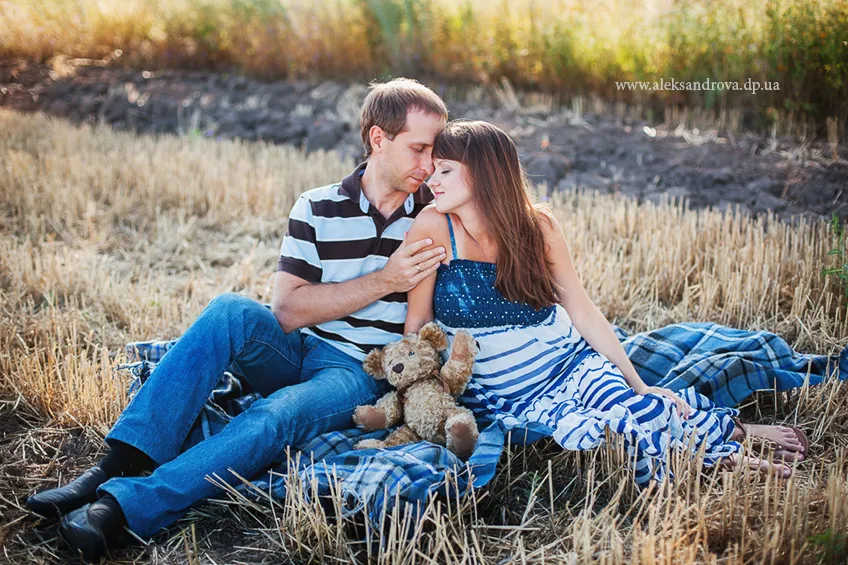 Expectant couple lying on a blanket with a teddy bear