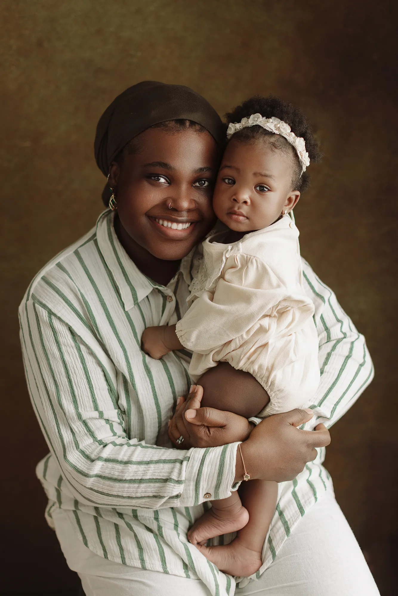 Mum holding her daughter in a cream outfit against a brown backdrop
