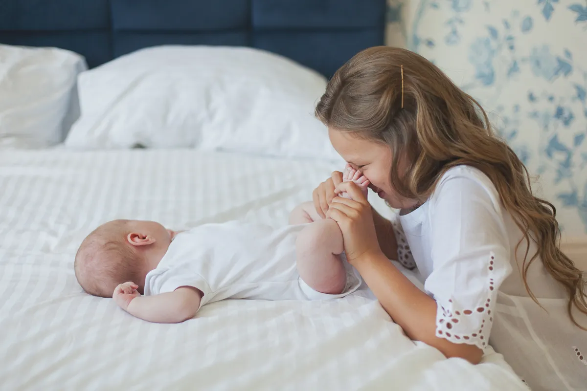 Girl kissing her newborn sibling's feet on a white bed