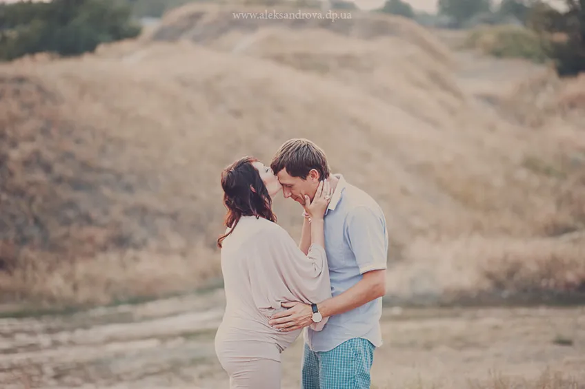 Expectant couple kissing in a golden landscape