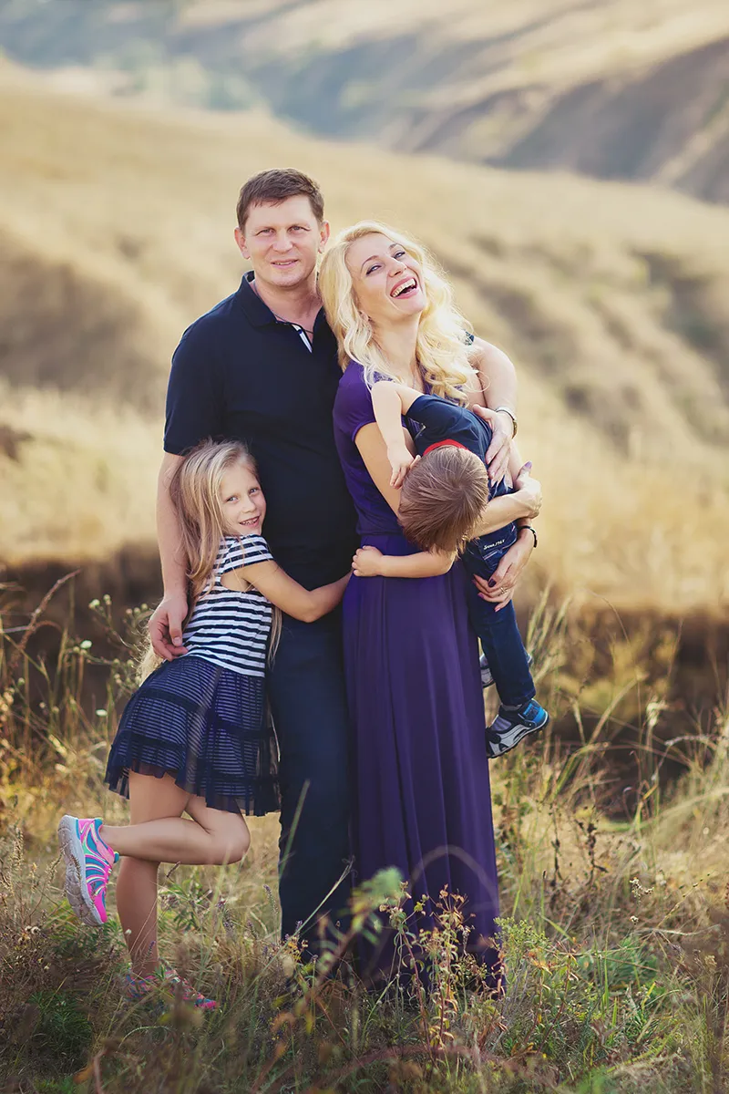Family of four hugging and laughing in a sunlit meadow