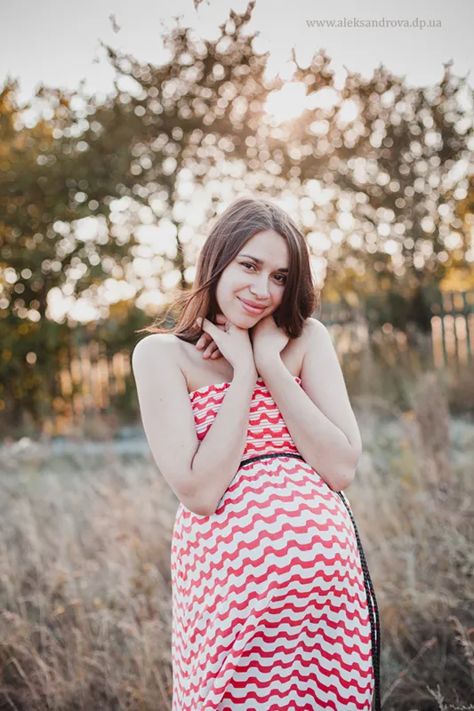 Pregnant woman in a red and white chevron dress in a garden at sunset