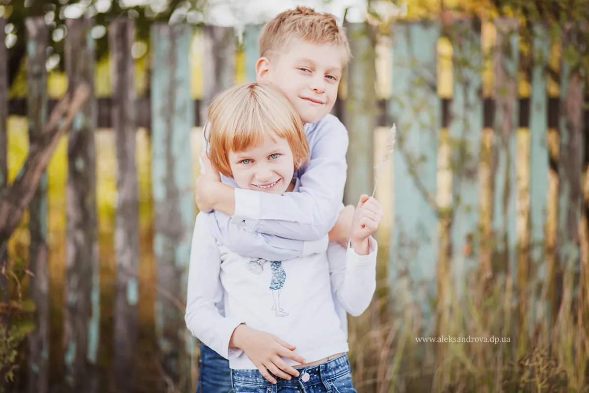 Two brothers hugging by a wooden fence