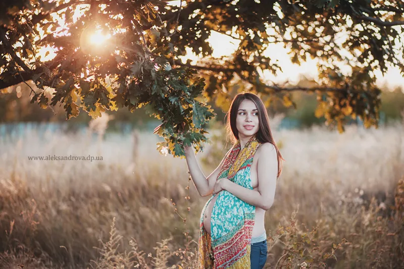 Pregnant woman in a colourful scarf standing under an oak tree