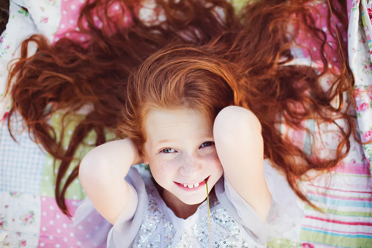 Laughing girl with red hair spread out on a patchwork quilt