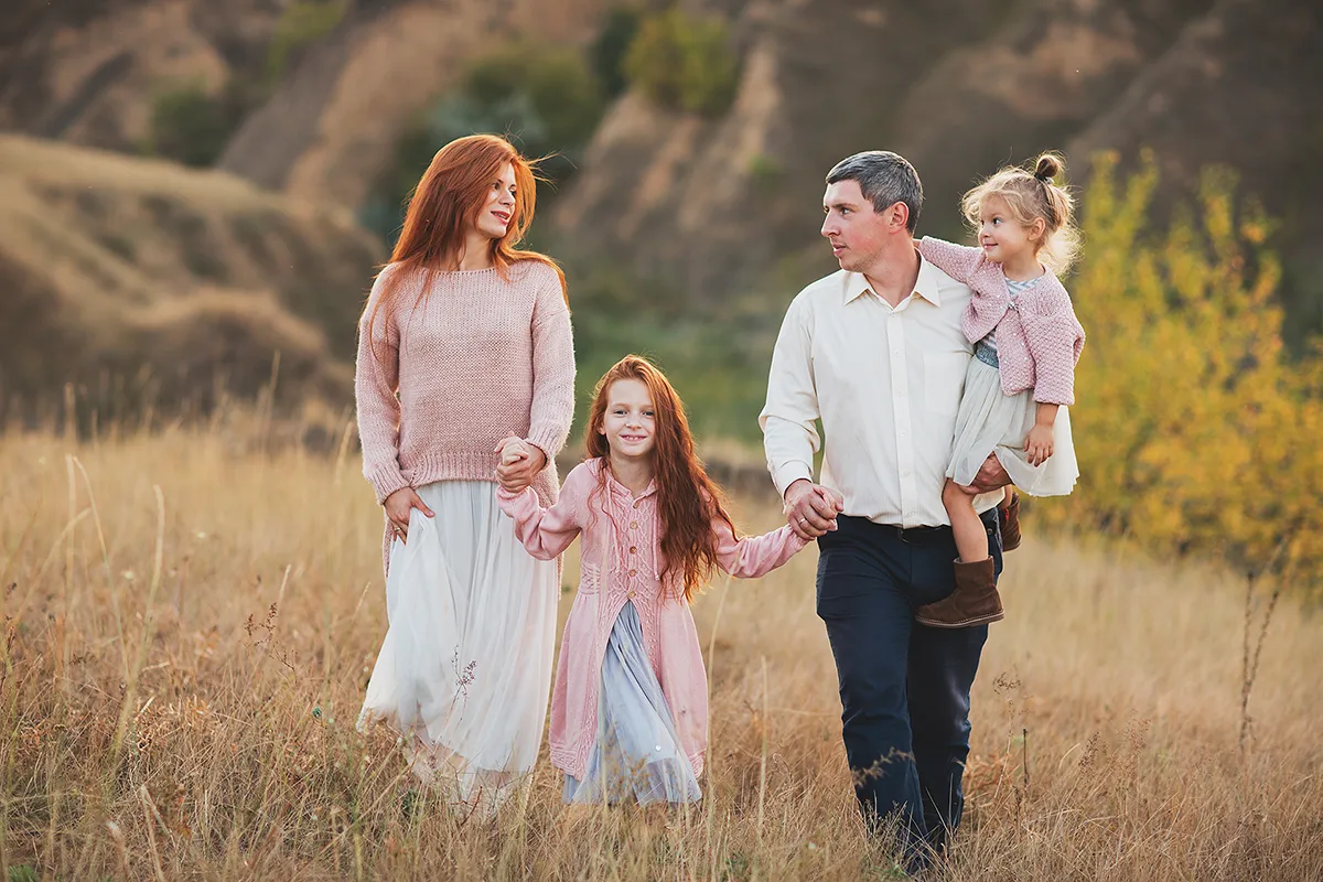 Family walking together through a golden field, dad carrying the youngest
