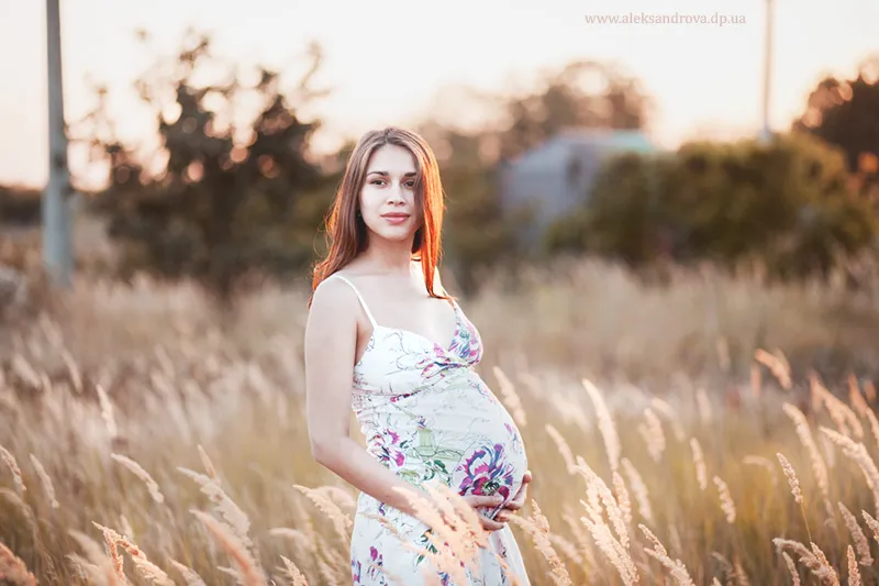 Pregnant woman in a floral sundress standing in a field of grasses