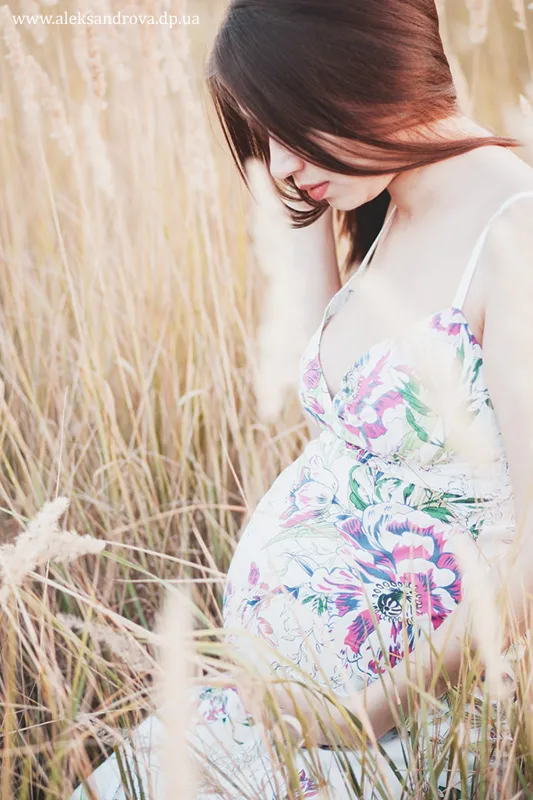 Close-up of a pregnant woman in a floral dress among tall grasses