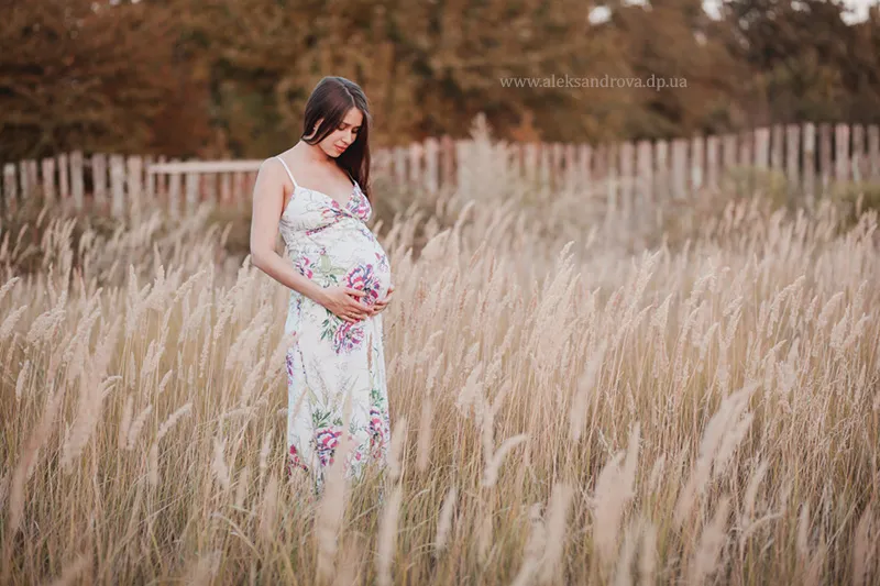 Pregnant woman in a floral dress in a meadow of feather grass