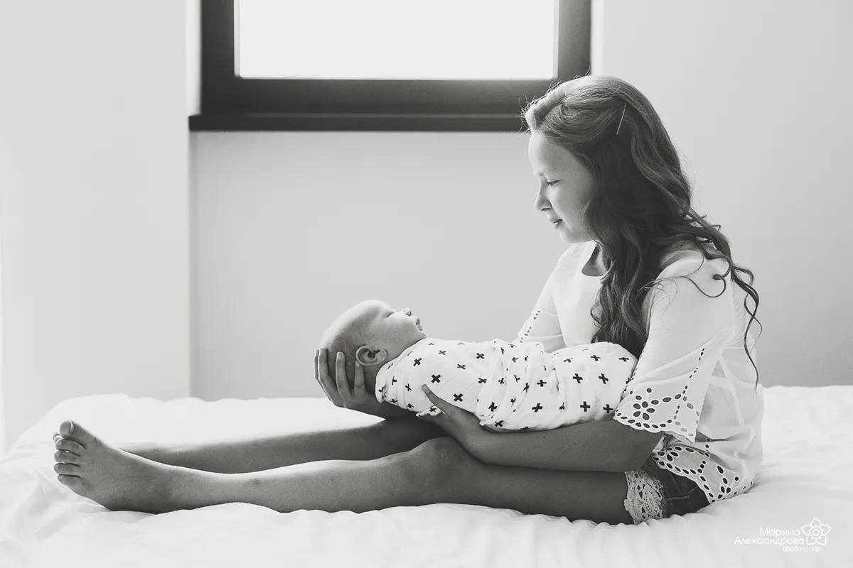 Black and white photo of a mother holding her baby on her knees on a bed