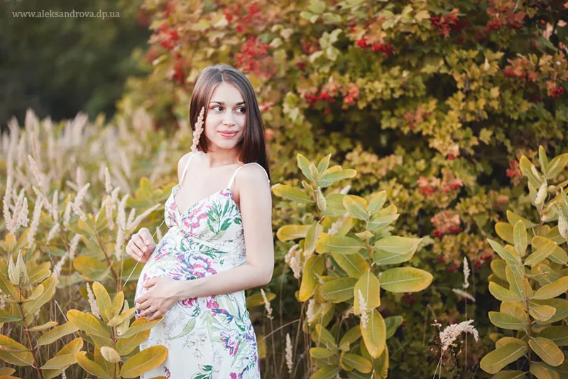 Pregnant woman in a floral dress in a colourful autumn garden