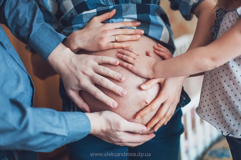 Family hands resting together on a pregnant belly