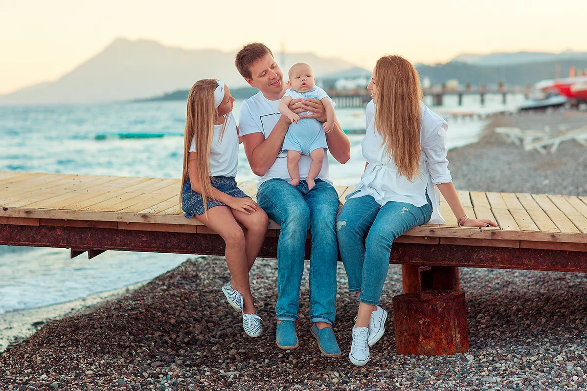 Family with a baby sitting on a wooden pier by the sea