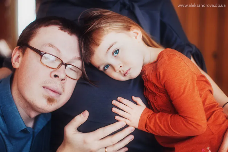 Dad and son resting their heads on mum's pregnant bump