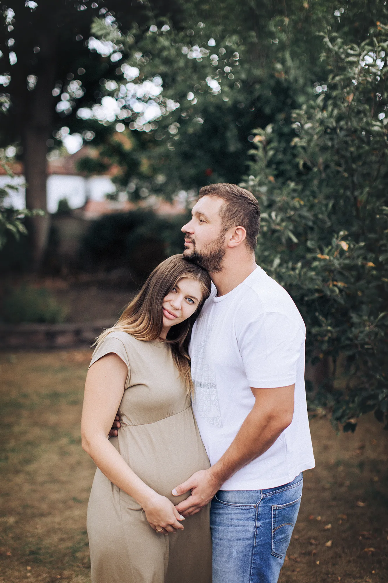 Expectant couple embracing in an orchard, hands on the bump