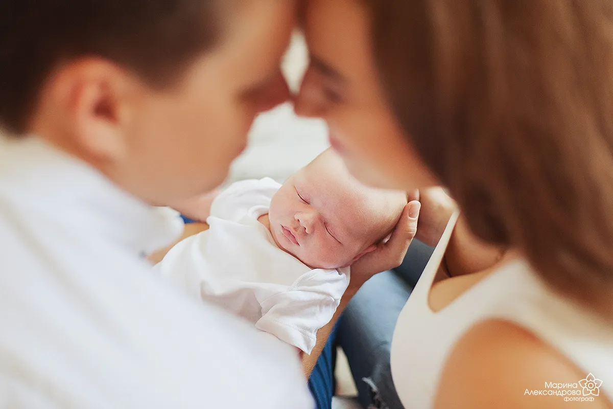 Parents' faces touching over their sleeping newborn