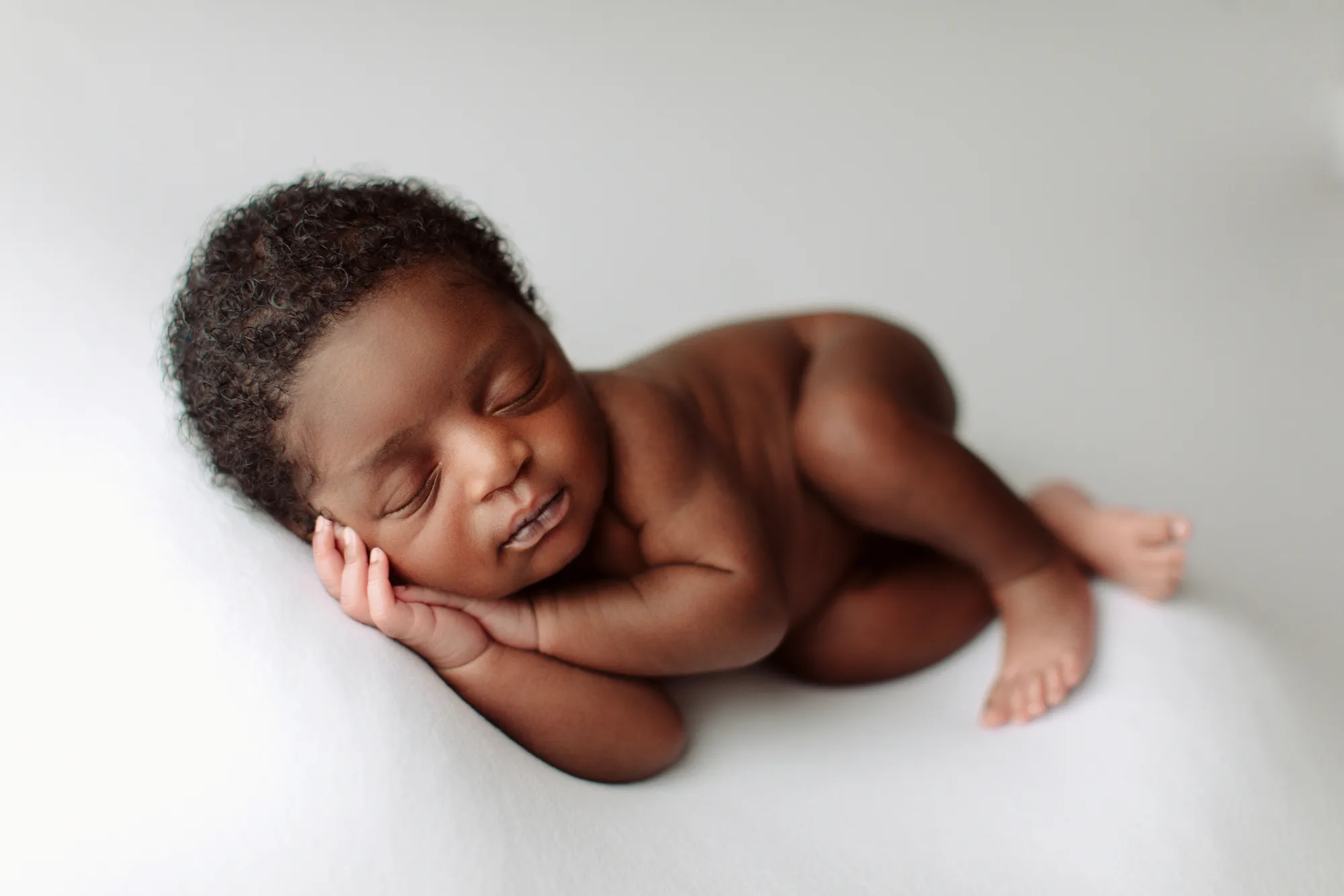 Newborn baby sleeping on a white backdrop with hands under cheek