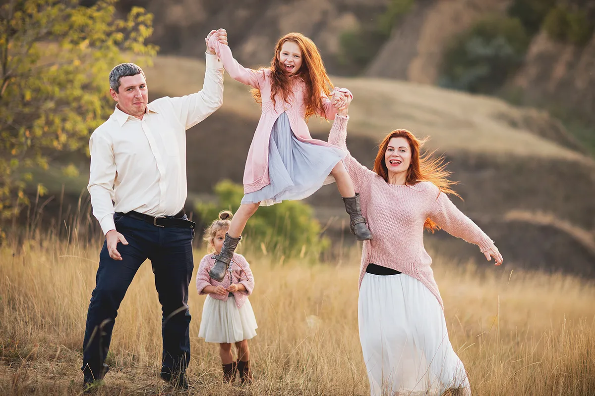 Family jumping and swinging their children in a meadow