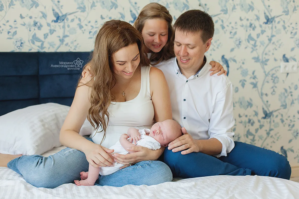 Parents and big sister admiring a newborn on a bed at home