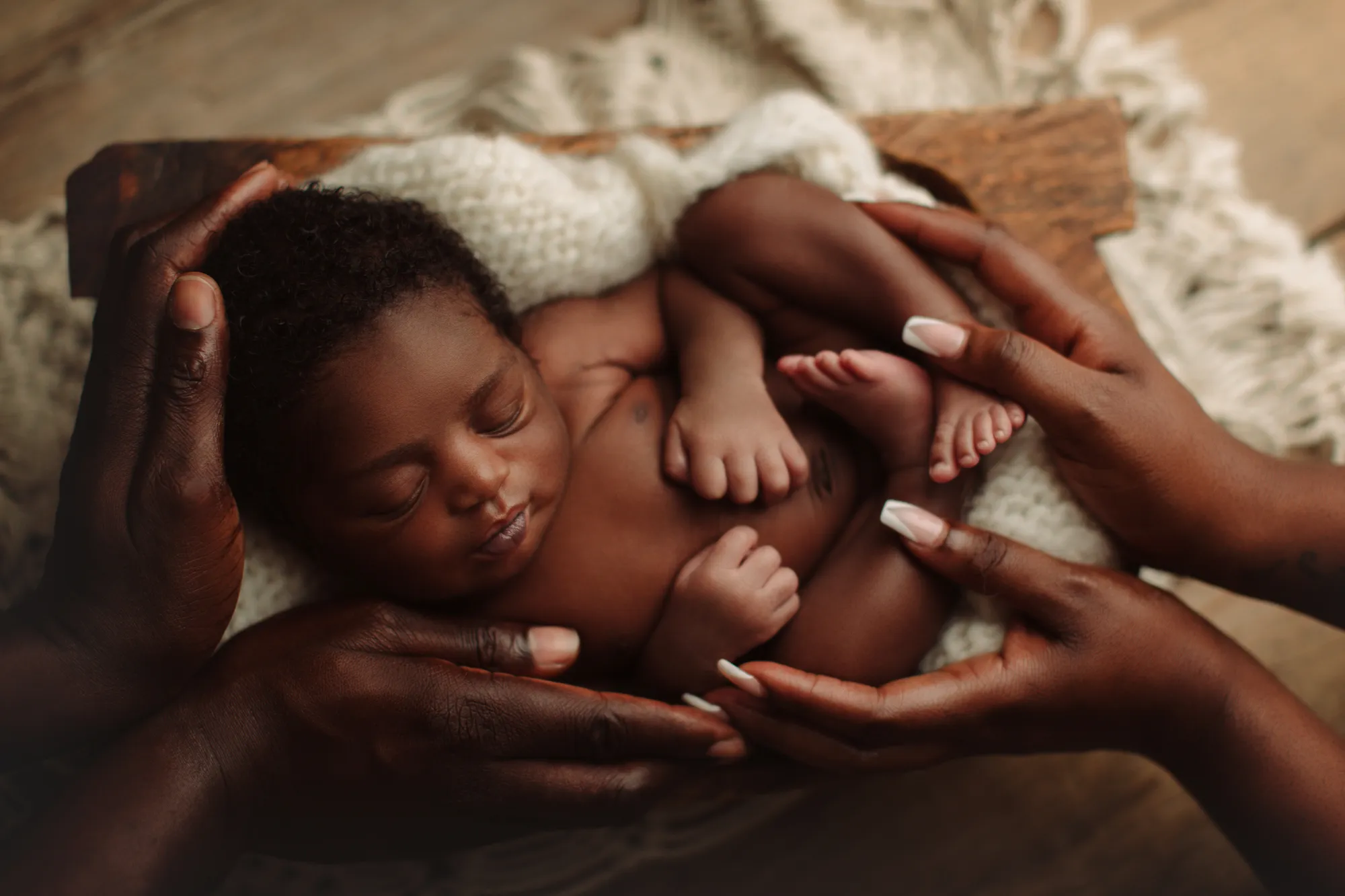 Parents' hands cradling their sleeping newborn on a knitted blanket