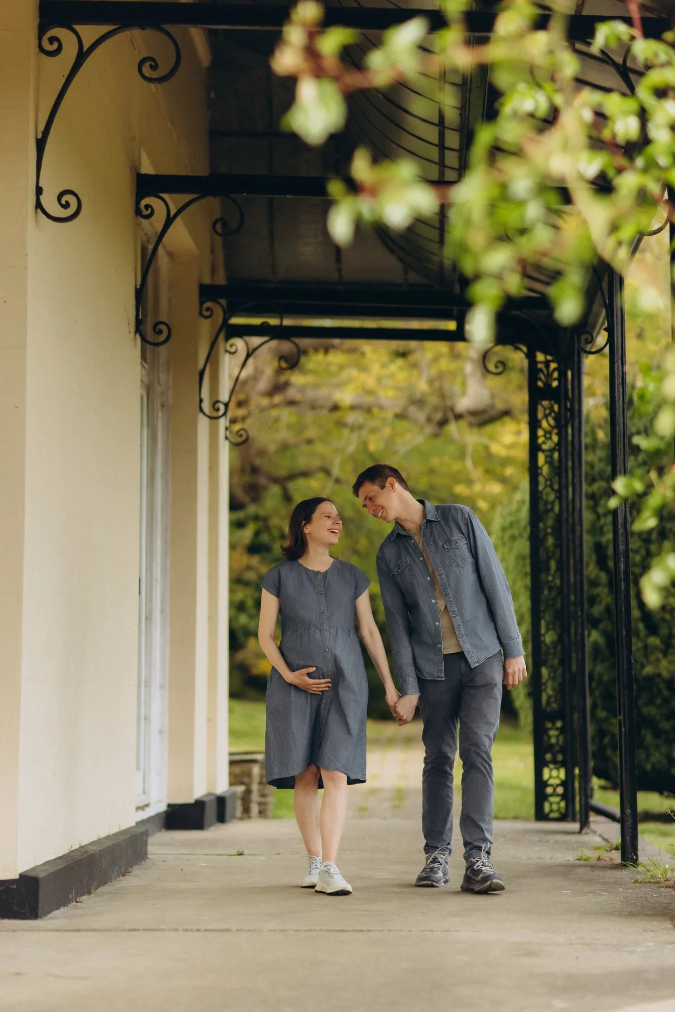 Expectant couple holding hands under a wrought-iron veranda