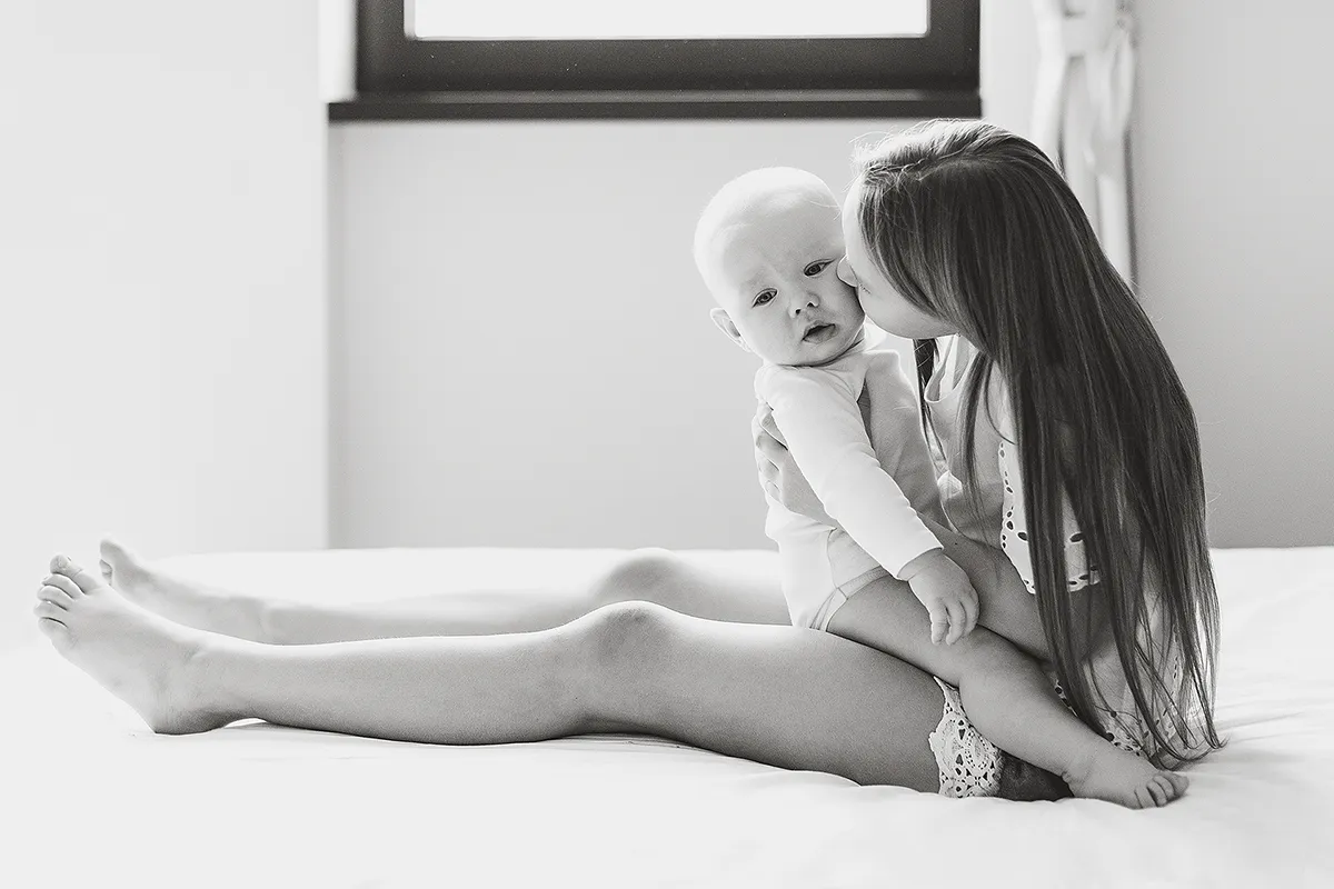 Black and white photo of a mother kissing her baby on a bed