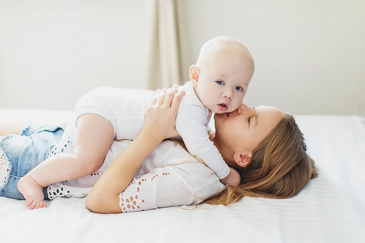 Mother lying on a bed kissing her baby son
