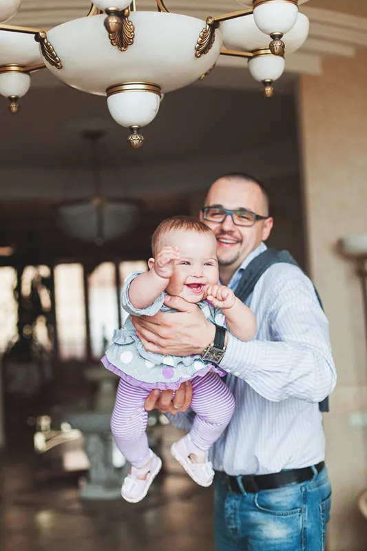 Dad holding up his laughing baby daughter in a grand hallway