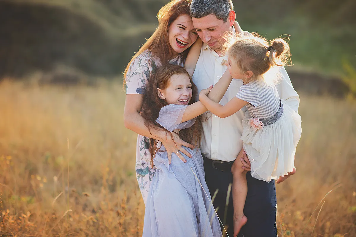 Mum and dad hugging their two daughters in a golden field