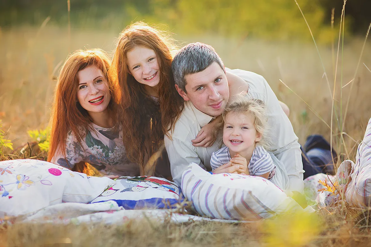 Family lying together on a blanket in tall summer grass